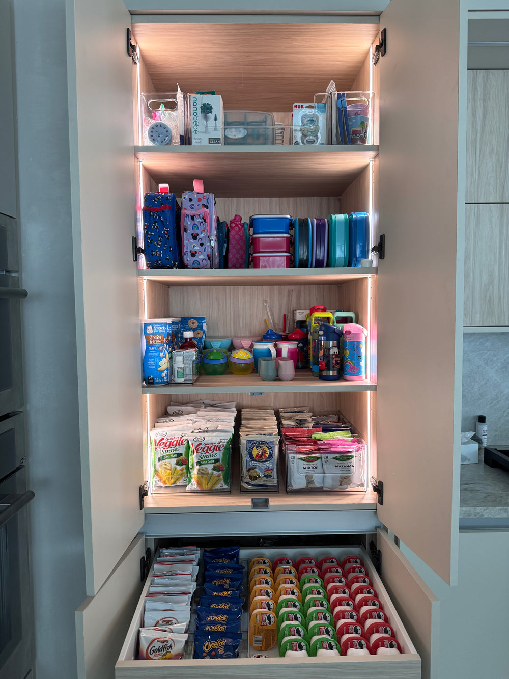 Gabinete de cocina con loncheras, vasos y meriendas de los niños organizados
